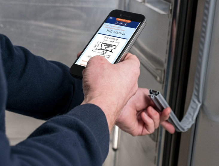 A photo of a man looking at a cross-section of a fridge seal, still attached to a fridge, and comparing it to a graphic on his phone.