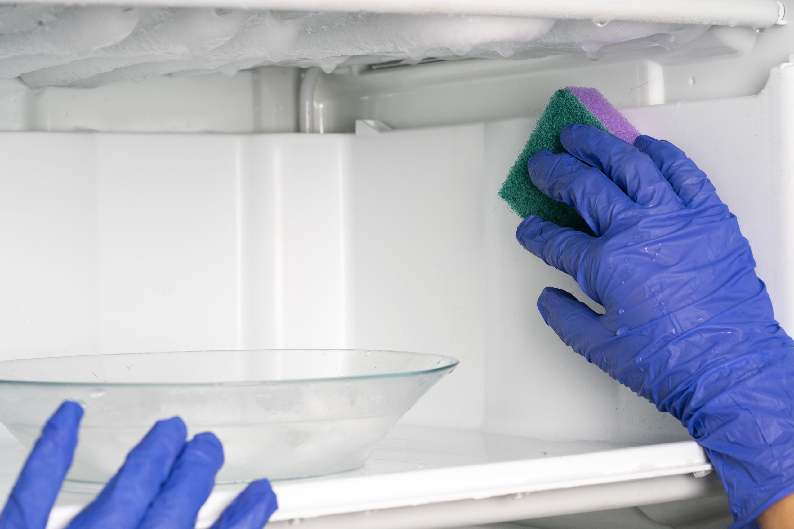 hands cleaning the fridge freezer during manual defrosting process