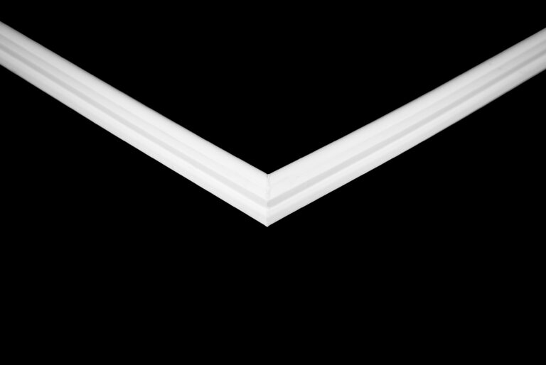 The Trimco Tavira II 1000 features a sharp white V-shaped moulding set against a solid black background, offering a minimalist and geometric look with bold lines converging at the centre.